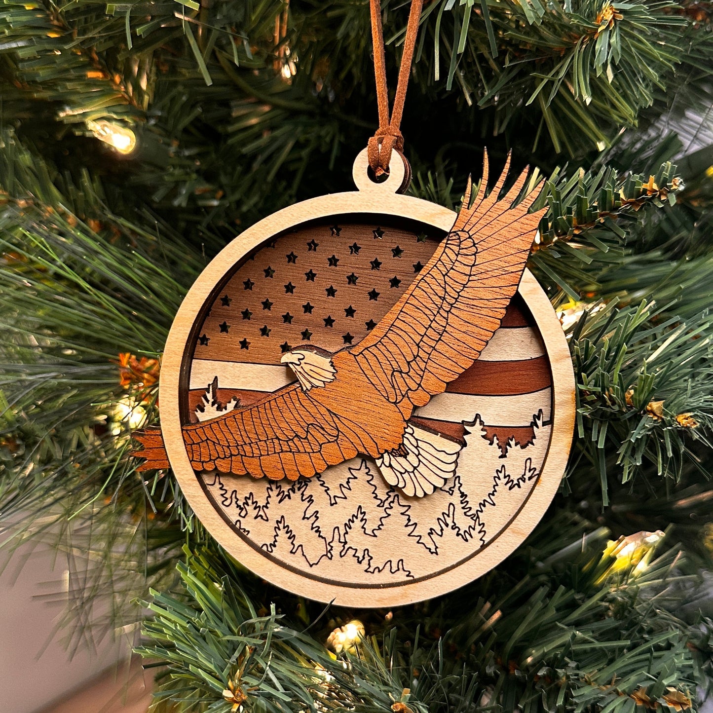 Layered wooden eagle flying over the trees with an American flag in the back ornament made with multiple species of wood.