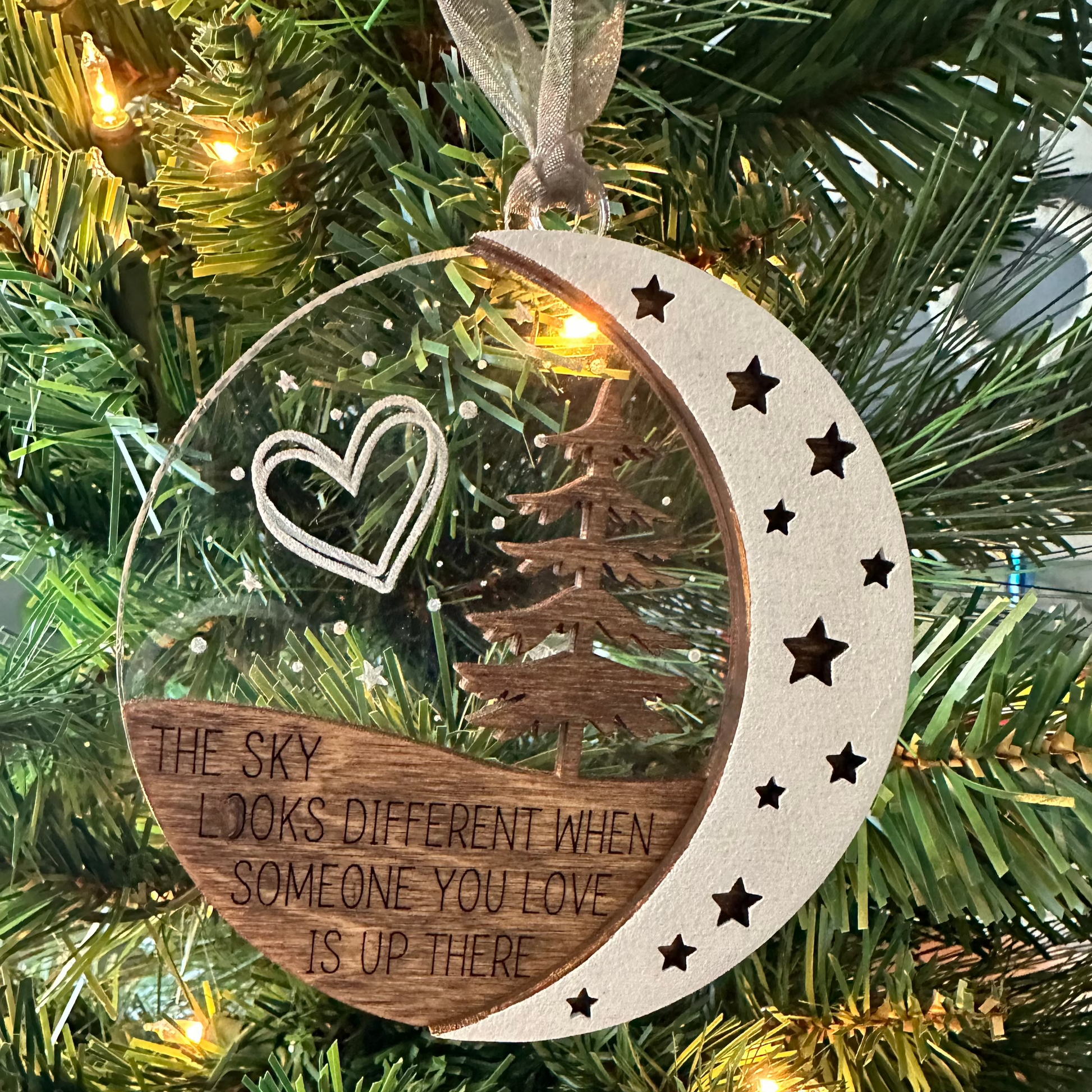 Three layered ornament that says the sky looks different when someone you love is up there. Clear acrylic backer to emulate the evening sky with stars and double heart engraved. Evergreen tree and moon in the for front. 